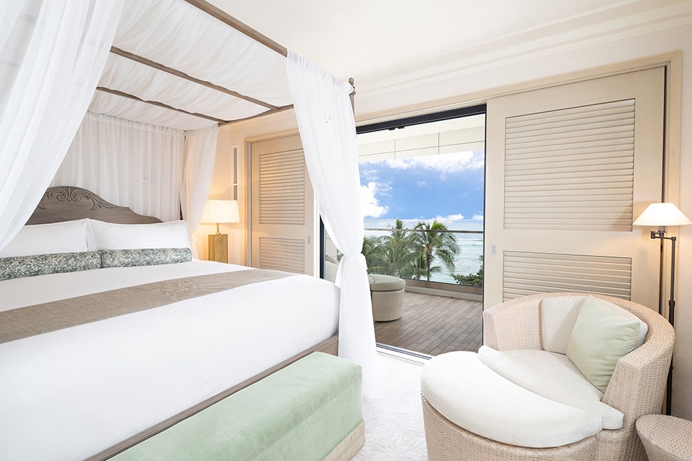 Room with canopy bed, seating, and balcony with ocean views.