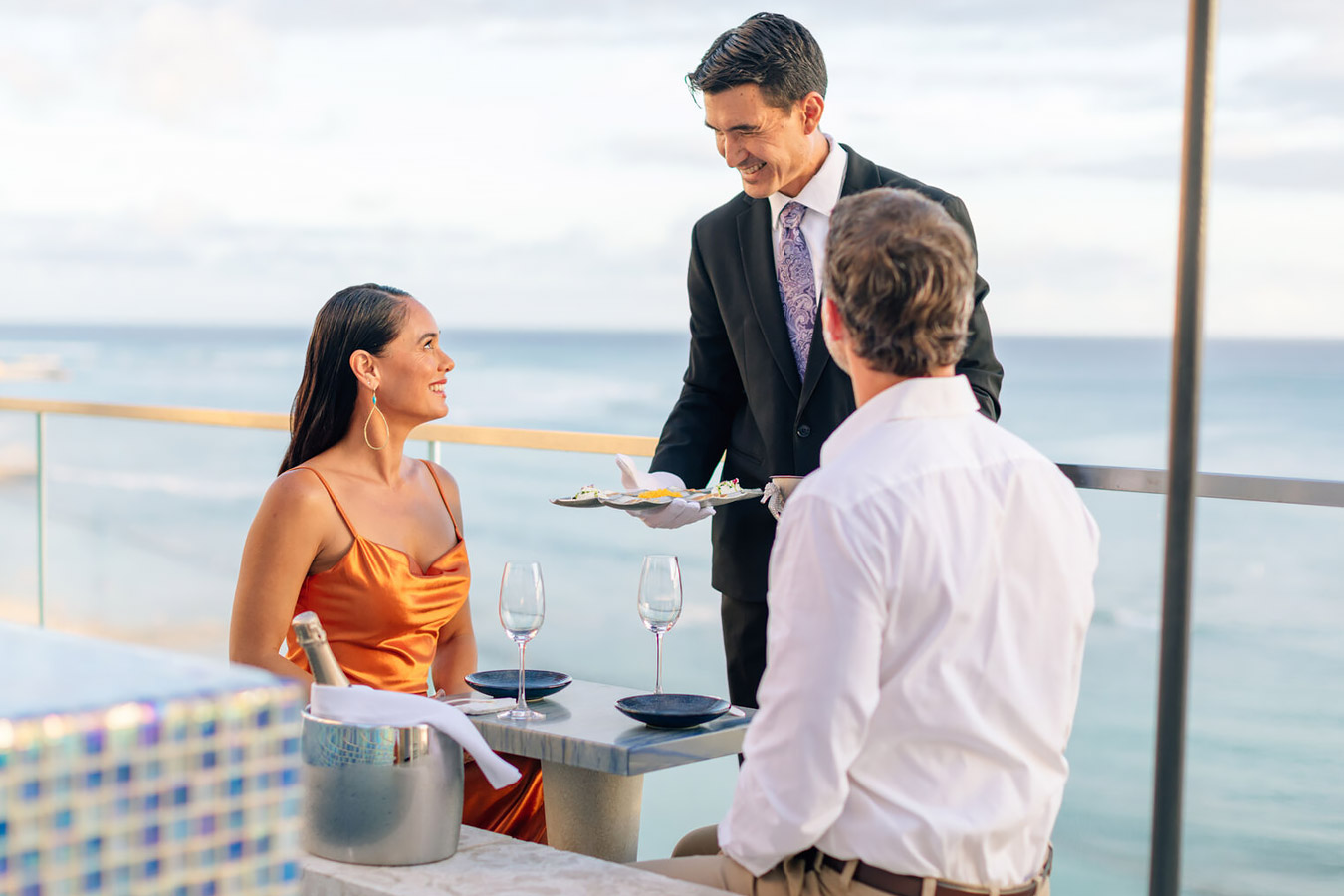 Couple being served champagne on the rooftop deck at ESPACIO with ocean in the background.