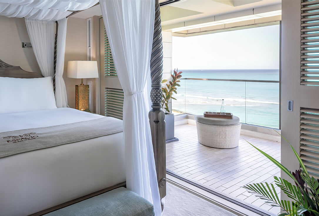 Room with a canopy bed, lamp, and balcony with ocean views.